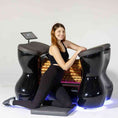 Load image into Gallery viewer, Woman sitting on a futuristic black chair with glowing blue accents against a white background
