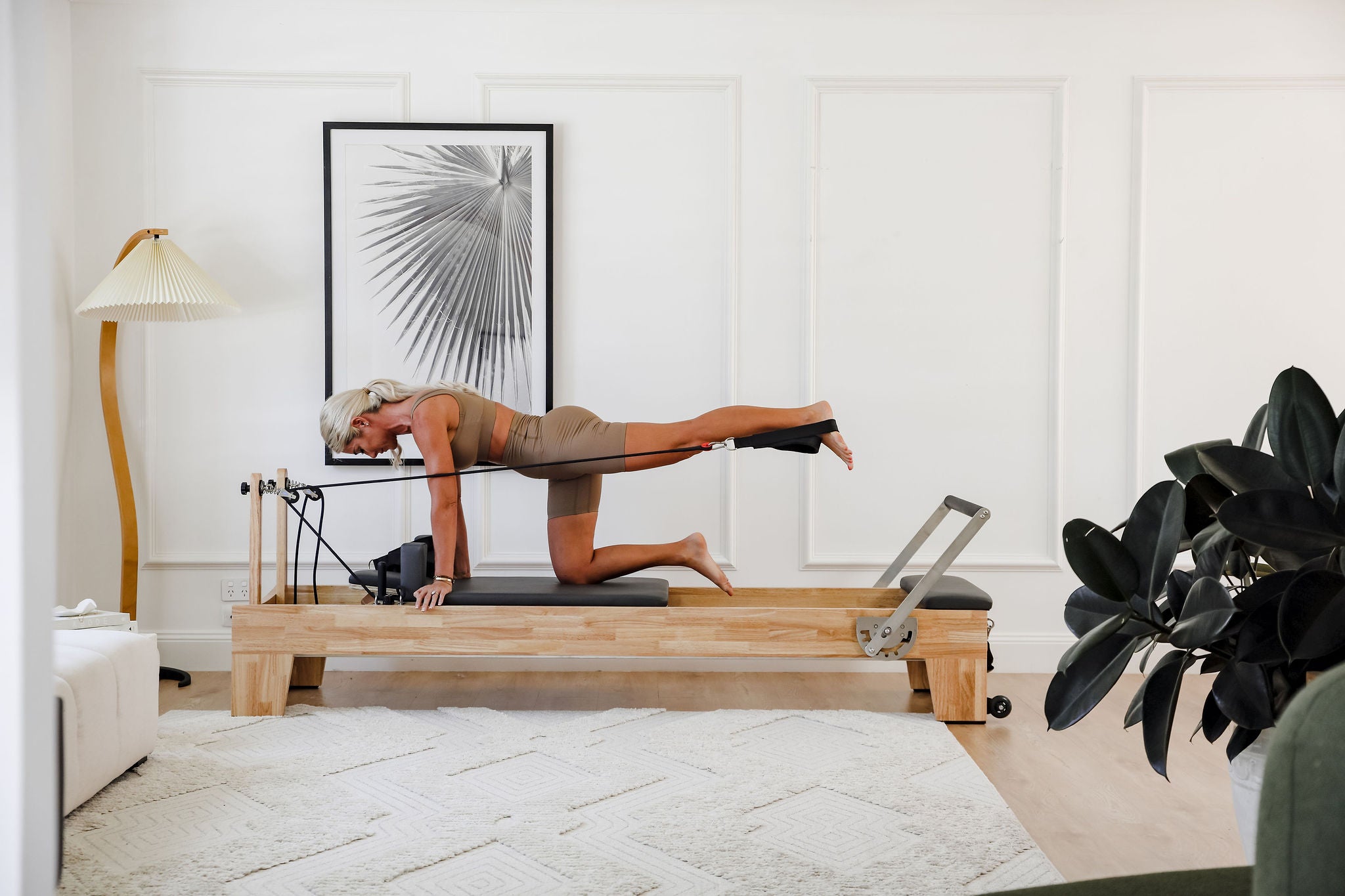 Person using a Pilates reformer machine in a home setting with decor elements.