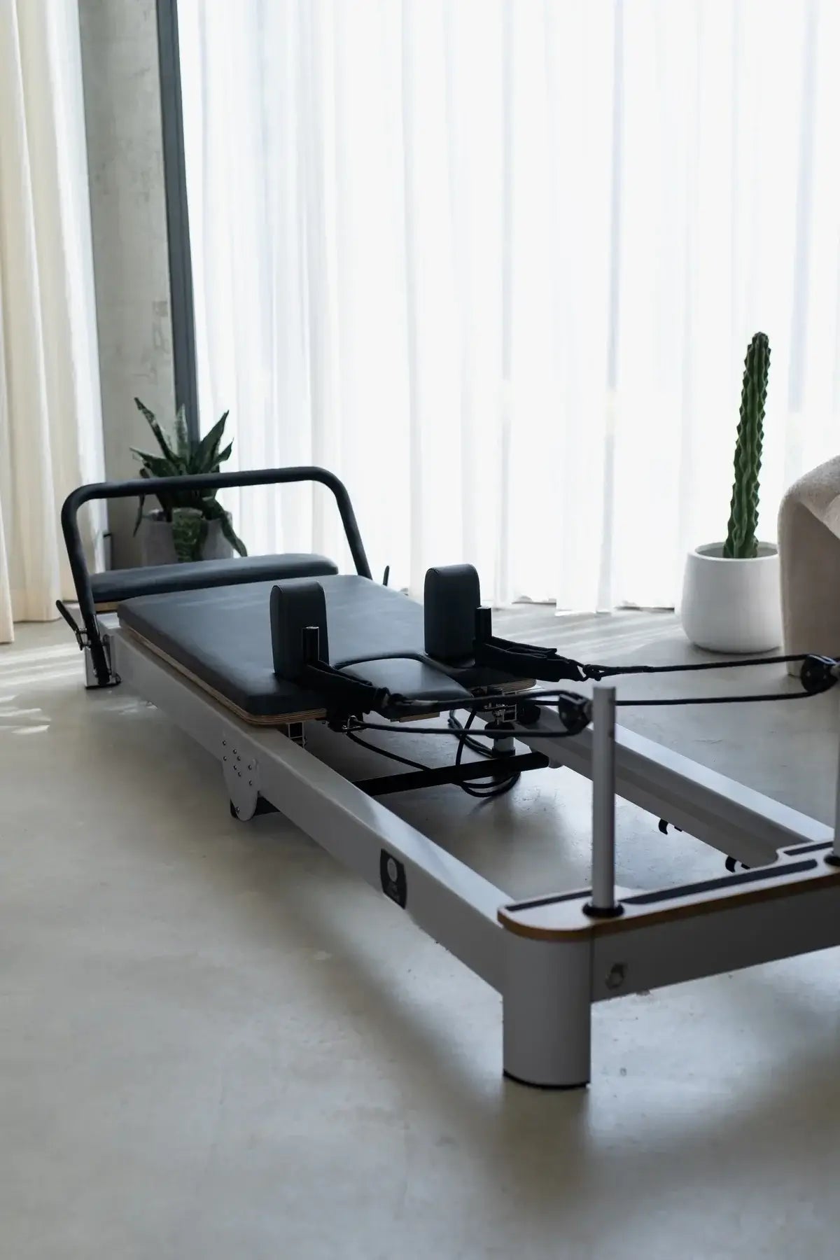 Pilates reformer machine in a room with large windows and plants.