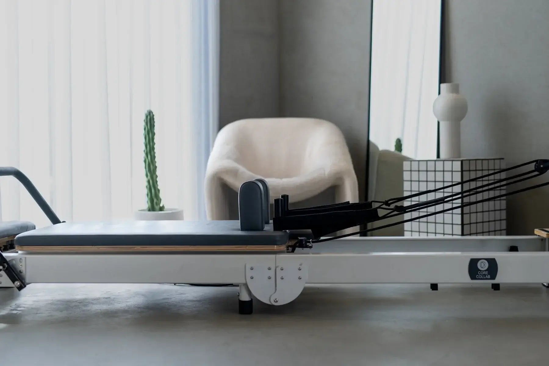Reformerc fitness machine in a modern room with a chair and plant.